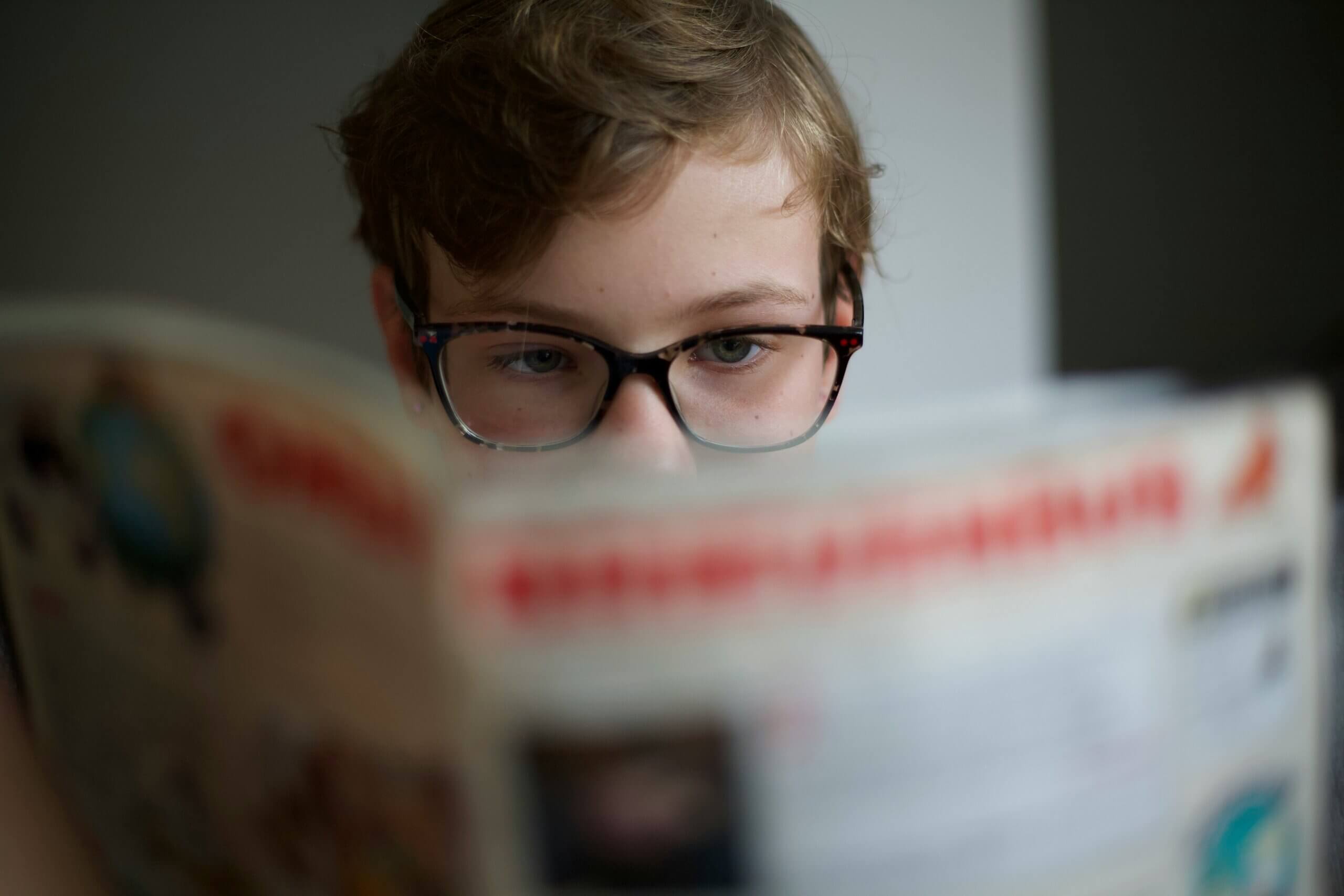 Young boy reading magazine, his face partially shown; magazine title obscured